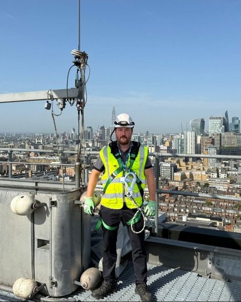 Mark Crowley, Director, on a rooftop BMU installation, with the City of London skyline behind